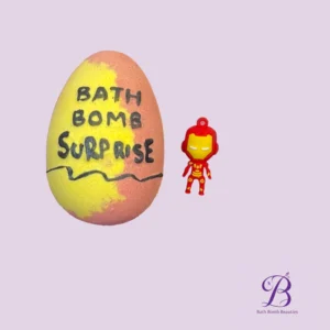 Two-toned yellow and pink bath bomb with the text 'BATH BOMB SUPPOSE' written on it, beside a small red Iron Man figure on a lavender background (Bath Bomb Beauties logo bottom right).