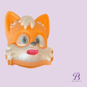 Orange fox-shaped bath bomb with white frosting face on a pale lavender background.