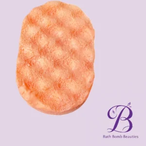 Peach colored exfoliating bath sponge with a textured surface on a lavender background featuring the bath bomb beauties logo in the corner