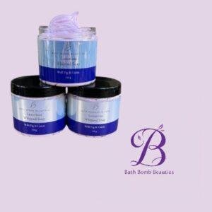 Three blue labeled jars of whipped soap stacked with a lavender tinted jar on top set on a light purple background with the bath bomb beauties logo visible to the right