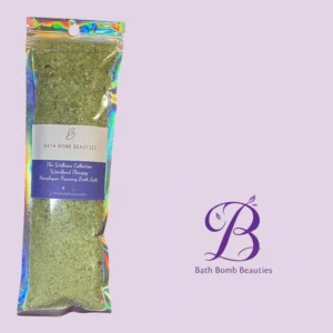Holographic bag of bath bomb beauties himalayan foaming bath salts on a lavender background label reads the wellness collection woodland therapy
