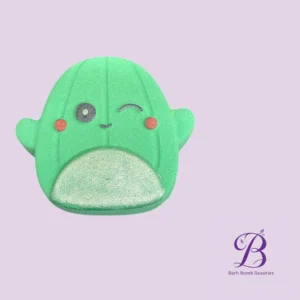 Cute green bath bomb shaped like a friendly character with a winking eye and rosy cheeks on a lavender background; Bath Bomb Beauties logo in corner.