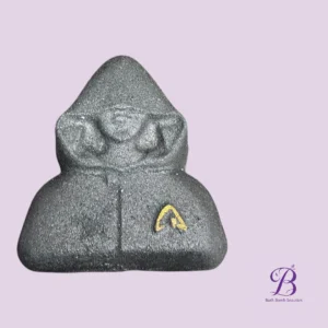 Gray hooded figure bath bomb with a small yellow emblem on the front, set against a lavender background.