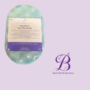 Aqua mistica soap filled sponge bath product in a blue green oval package on a lilac background with bath bomb beauties logo