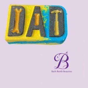 Close-up of a colorful stamped bath bomb block showing the letters 'DAT' on a pastel purple background, with a Bath Bomb Beauties logo in the corner.