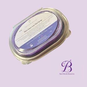 Close-up of a jar containing a purple bath bomb with a white label that reads Bikini Season Soap Filled Sponge, on a light lavender background.