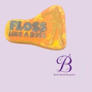 Orange and yellow bath bomb with the slogan 'FLOSS LIKE A BOSS' and a gold silhouette, placed above a purple Bath Bomb Beauties logo.