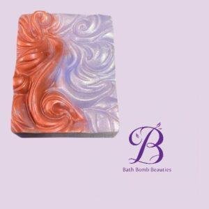 Marbled orange and lavender soap bar on a light lavender background with Bath Bomb Beauties logo in the bottom-right corner.