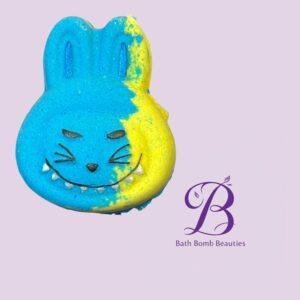 Blue and yellow smiling bunny bath bomb with a purple bath bomb beauties logo in the corner against a light purple background