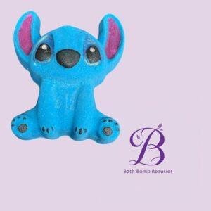 Blue Stitch-like plush toy with pink inner ears on a lavender background, Bath Bomb Beauties logo in purple bottom right.