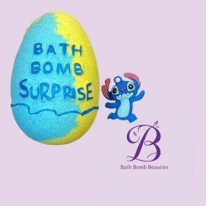 Colorful blue and yellow bath bomb with bath bomb surprise text beside a cute blue cartoon creature and bath bomb beauties logo on a lavender background