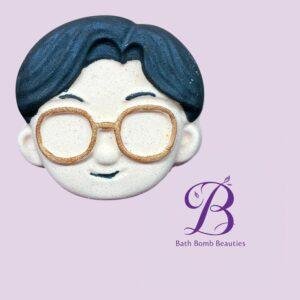 Ceramic head with blue hair and gold glasses on lavender background bath bomb beauties logo visible at side