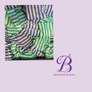 Assorted striped green and blue bath bomb wrappers in a box beside a purple bath bomb beauties logo on a lavender background