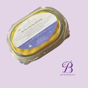 Jar containing a yellow bath bomb with a Bath Bomb Beauties label, set against a pale purple background.