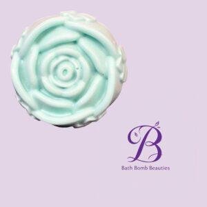 Close-up of a spiral mint-green bath bomb on a light purple background, featuring the Bath Bomb Beauties logo watermark in purple text.