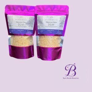 Two pink stand up pouches of bath bomb beauties magnesium flakes bath soak creamy matcha with a purple logo on a lavender background