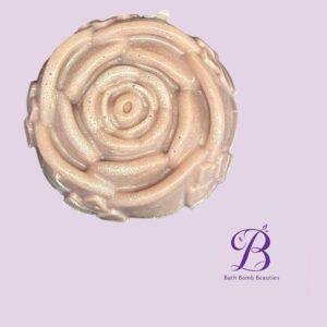 Close up of a pink rose shaped bath bomb with glitter on a light purple background bath bomb beauties logo visible