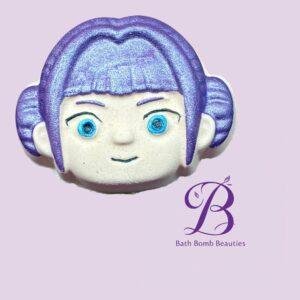 Close up of a purple haired cartoon face cookie on a lavender background with bath bomb beauties branding visible at the bottom right