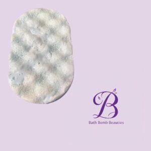 Pale textured bath bomb on a lavender background with a purple bath bomb beauties logo to the right