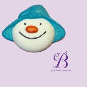 Snowman-shaped bath bomb with a blue hat and orange nose on a lavender background, featuring the Bath Bomb Beauties logo.