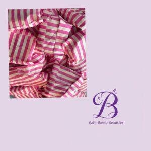 Pile of pink and white striped wrapped bath bombs on a lavender background with bath bomb beauties logo in purple