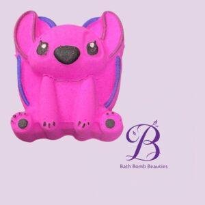 Pink dog-shaped bath bomb with purple ears and accents on a lavender background, featuring the Bath Bomb Beauties logo in the corner.