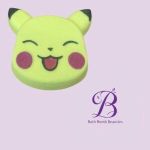 Yellow bear-shaped bath bomb with a smiling face and pink cheeks on a lavender background, beside the Bath Bomb Beauties logo.