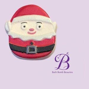 Santa-shaped bath bomb with red suit and white trim on a lavender background; branding reads Bath Bomb Beauties in the corner.