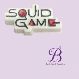 White d lettering spelling squid game on a pale purple background with a bath bomb beauties logo in purple at the bottom right