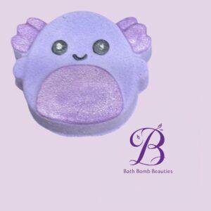 Purple bath bomb shaped like a cute creature with a glittery pink belly and small smile on a lavender background with the bath bomb beauties logo