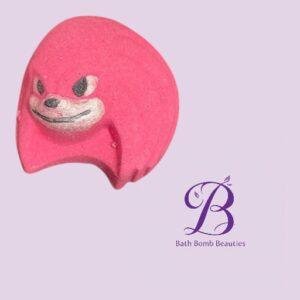 Pink bath bomb with a smiling cartoon face on a light purple background; shows the Bath Bomb Beauties logo in purple text and flourish.