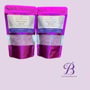 Two pink resealable pouches of bath bomb beauties magnesium flakes bath soak shown side by side on a lavender background with product labels facing forward