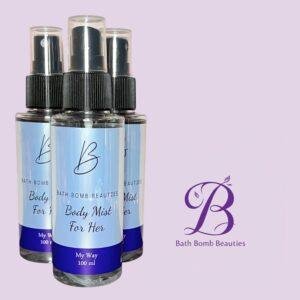 Three bath bomb beauties body mist spray bottles with blue labels and black caps arranged on a lavender background with a purple logo nearby