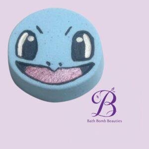 Blue bath bomb with a smiling face and pink glittery mouth on a pastel purple background, Bath Bomb Beauties logo in the corner.