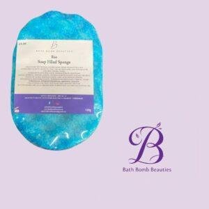 Blue soap filled sponge bath bomb labeled rio from bath bomb beauties displayed on a lavender background with the brand logo visible