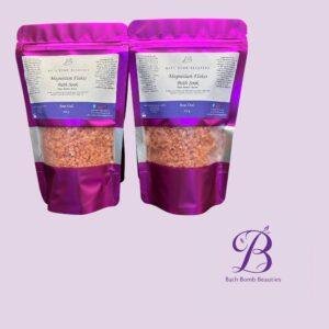 Two pink resealable pouches of bath bomb beauties magnesium flakes bath soak rose oud shown side by side with a decorative logo in the corner against a light purple background