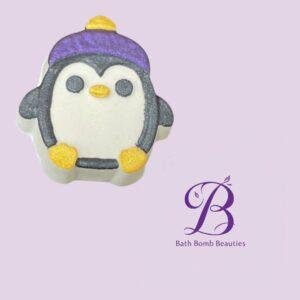 Penguin-shaped bath bomb with a purple hat and yellow feet on a lavender background, featuring the Bath Bomb Beauties logo.