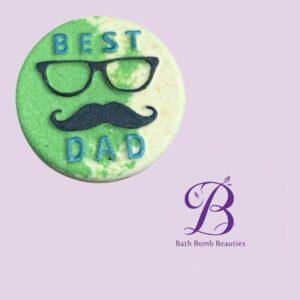 Round bath bomb with green and white swirls, 'BEST DAD' and a mustache design on a lilac background (Bath Bomb Beauties branding).