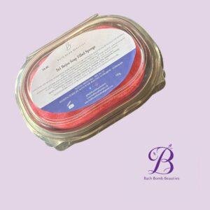 Close-up of a jar containing a red bath bomb with a label that reads 'Bath Bomb Beauties' on a lavender background.