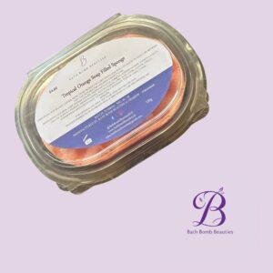 Jar with an orange bath bomb and a white label reading 'Bath Bomb Beauties' on a lavender background (brand product photo).