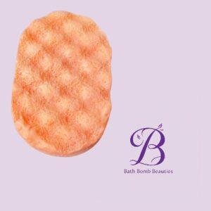Orange oval textured bath bomb on a pale lavender background with the bath bomb beauties logo in the bottom right corner