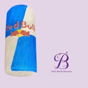 Blue-and-white cylindrical bath bomb with a Red Bull logo, set on a lavender background with Bath Bomb Beauties branding nearby.
