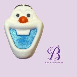 Close-up of a white snowman bath bomb with orange nose and blue interior, on a lavender background with Bath Bomb Beauties logo.