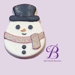 Snowman-shaped bath bomb with a dark hat, orange nose, pink scarf, and Bath Bomb Beauties logo on a lavender background.