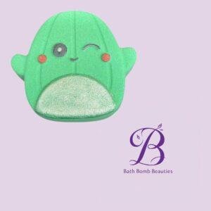 Green ghost shaped bath bomb with a cute face on a pastel purple background featuring bath bomb beauties logo in the corner