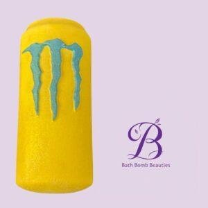 Cylindrical bright yellow bath bomb with blue drip design on a pale purple background, featuring the Bath Bomb Beauties logo nearby.
