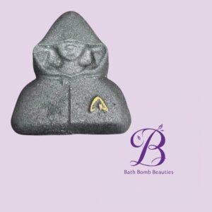 Gray buddha shaped bath bomb with a small gold logo set against a lavender background with bath bomb beauties branding
