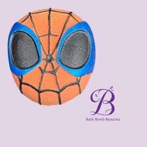 Bath bomb shaped like Spider-Man mask (orange with blue eye outlines) on a lavender background with Bath Bomb Beauties logo visible.