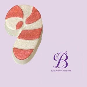 Foot-shaped bath bomb with pink and white stripes on a lavender background, featuring the Bath Bomb Beauties logo in purple.