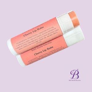Cherry lip balm bath bomb beauties Two pink cherry lip balm tubes crossed on a lavender background with a bath bomb beauties logo in the bottom right corner
